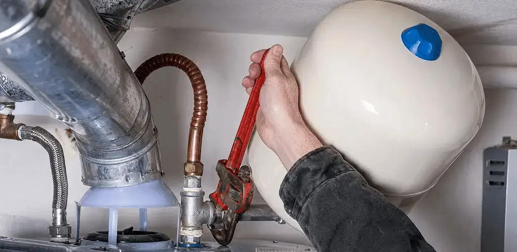 Water heater repair technician tightening plumbing connections near a tank unit in Denver, CO